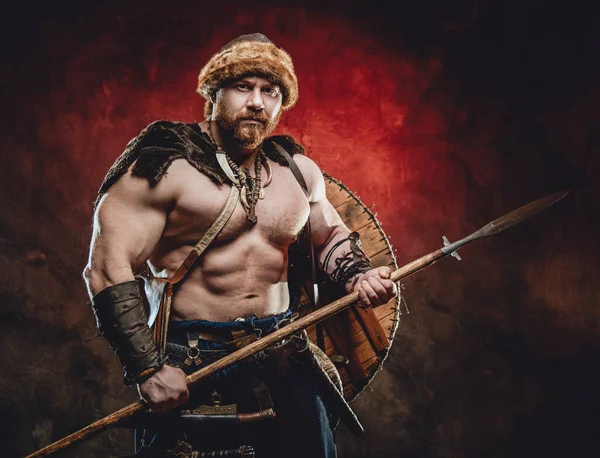 Handsome northern barbarian with spear in dark red background — Stock Photo, Image