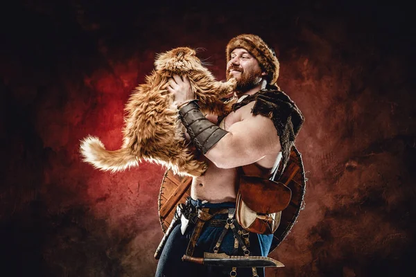 Guerreiro viking alegre brincando com gato no fundo escuro — Fotografia de Stock