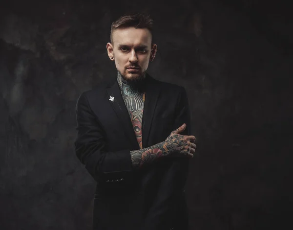 Tattooed serious guy in jacket with stylish haircut in dark background — Stock Photo, Image