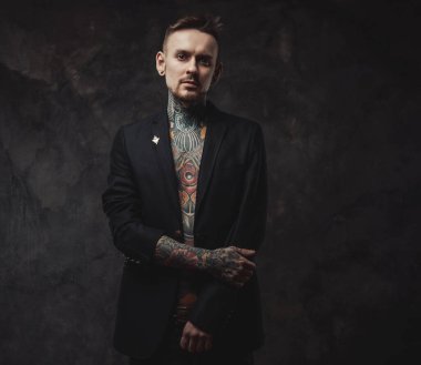 Siyah ceketli ciddi bir hippi karanlık arka planda kameraya bakıyor.