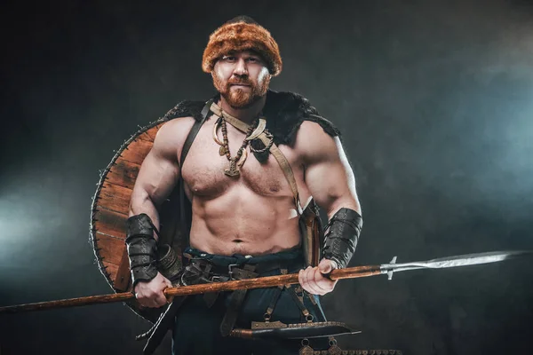 Vikingo sin camisa armado con lanza posa en un fondo ahumado — Foto de Stock