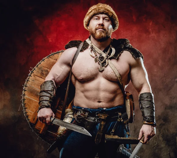 Çıplak gövdeli kaslı viking ve koyu kırmızı arka planda bıçaklar. — Stok fotoğraf