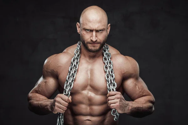 Serious and handsome guy poses in dark background with heavy chains — Stock Photo, Image