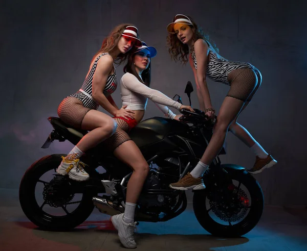 Vackra flickor i korta kläder och mössor poser med motorcykel — Stockfoto