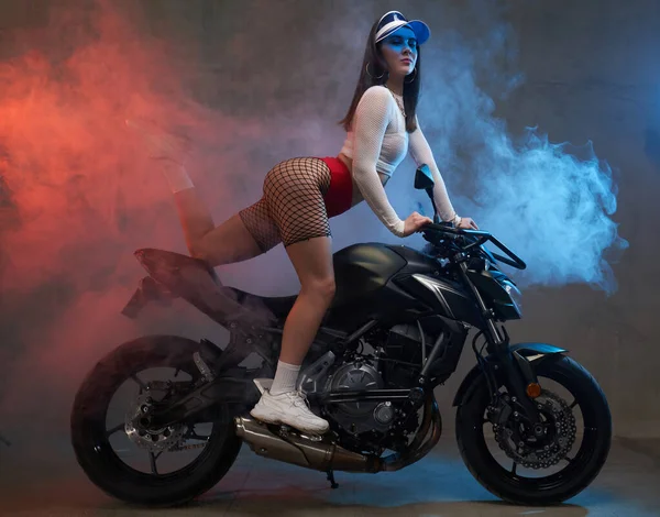 Graciös sexig tjej med mössa poserar på anpassad motorcylce i studio — Stockfoto