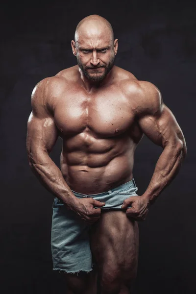 Wütender Bodybuilder mit Glatze zieht seine Shorts und zeigt sein muskulöses Bein — Stockfoto