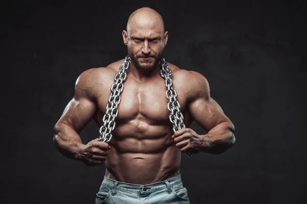 Seriöser haarloser Bodybuilder posiert mit Stahlketten im dunklen Hintergrund — Stockfoto