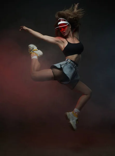 Žena tanečnice s červenou čepicí skákání v tmavém kouři pozadí — Stock fotografie