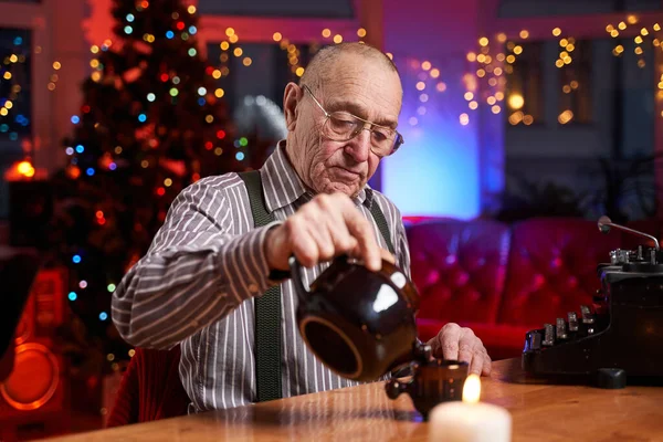 Beber um ancião do chá quente sentado à mesa em quarto colorido — Fotografia de Stock