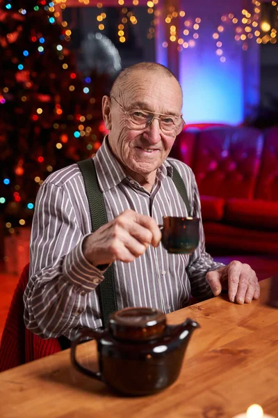 Beber um ancião do chá quente sentado à mesa em quarto colorido — Fotografia de Stock