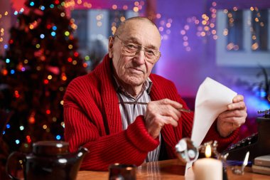 Noel Baba renkli bir odada oturmuş Noel kartları yazıyor.