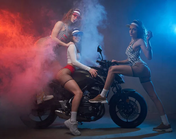 Спортивные девушки позируют на велосипеде в красочной туманной студии — стоковое фото