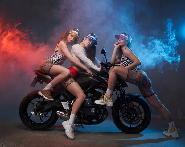 Ragazze allegre in abiti sexy pose sulla moto in studio — Foto Stock
