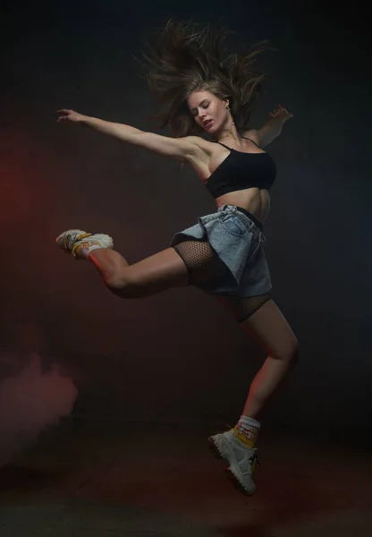 Стрибки жіночої танцівниці в короткому одязі на темному фоні — стокове фото