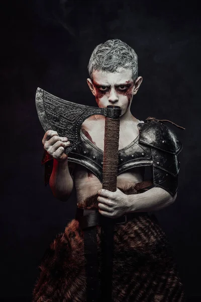 Holding an axe little barbarian with painted skin in dark background — Stock Photo, Image