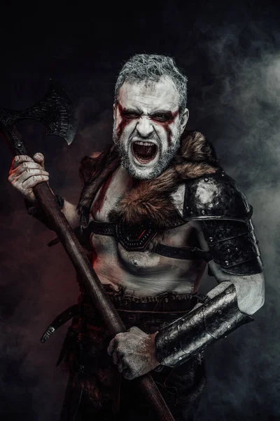 Screaming mythical warrior with painted skin and axe in studio — Stock Photo, Image