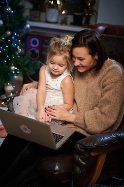Mutlu anne ve kızı koltukta oturup dizüstü bilgisayara bakıyorlar.