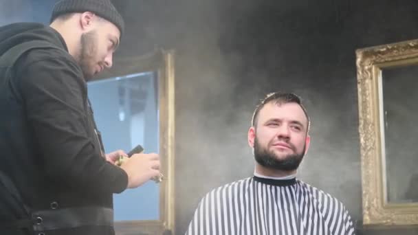 검은 색 콜로세움을 입고 스모키와 스타일링 룸에서 고객의 머리를 면도하고 있는 칸막이 이발사 — 비디오