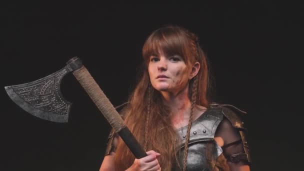 Utilizando un hacha enorme mujer bárbara y escandinava en armadura posando en un fondo oscuro — Vídeos de Stock