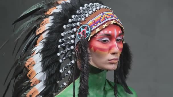 Modelo femenino con piel pintada y tocado indio posa en fondo oscuro — Vídeos de Stock