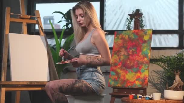 Красивая женщина-дизайнер смешивает краски на палитре с кистью в комнате — стоковое видео