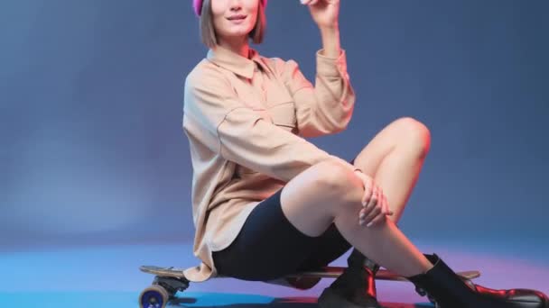 Joyeux modèle féminin avec chapeau rose assis sur planche à roulettes — Video