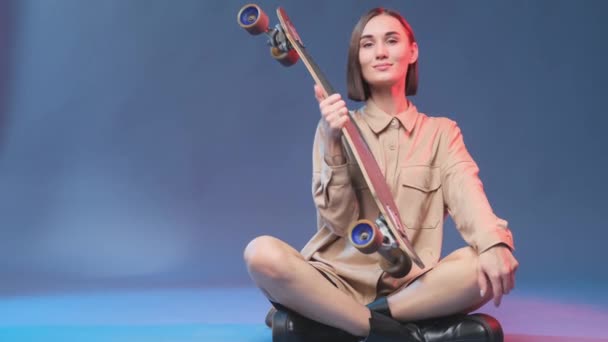 Joyeux et souriant hipster girl avec planche à roulettes en fond bleu — Video