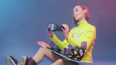 Snowboard 'lu şık sporcu kadın stüdyoda göz giysisi giyiyor.