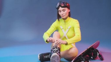 Çekici sporcu kadın ayakkabı bağcıklarını mavi arka planda hazırlıyor ve bağlıyor.