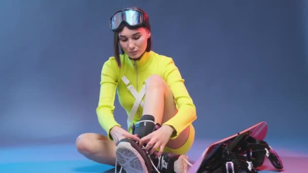 Verführerisches Mädchen in gelber Sportbekleidung bindet ihre Schnürsenkel vor blauem Hintergrund — Stockvideo