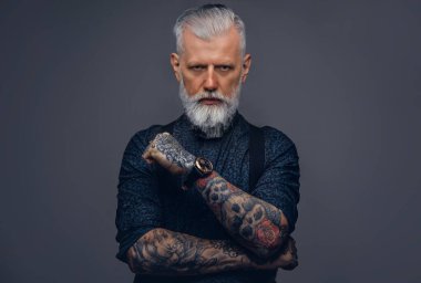 Stüdyoda kameraya bakarak poz veren şık giyimli zalim yaşlı bir adam.