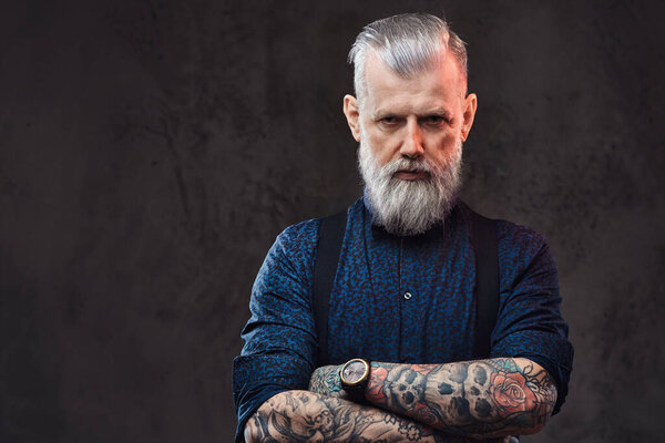 Жестокий старик с татуированными руками смотрит в камеру на тёмном фоне.