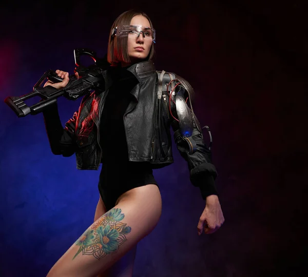 Futurista mujer cibernética sosteniendo rifle en estudio oscuro y atmosférico — Foto de Stock