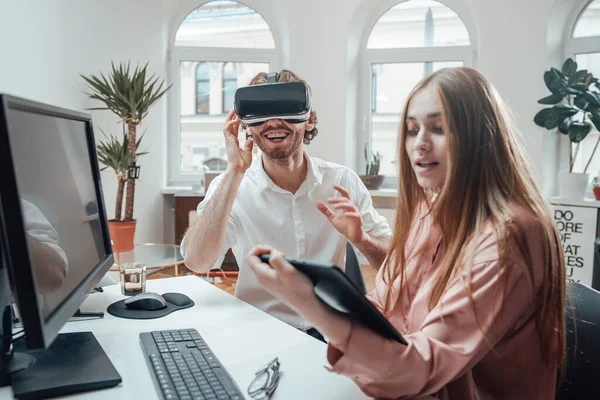 Vidám fickó élvezi a virtuális valóság szemüveg, míg a partnere dolgozik tabletta — Stock Fotó