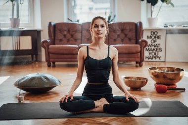 Loto pozisyonunda halının üzerinde neşeli bir kadın oturma odasında.