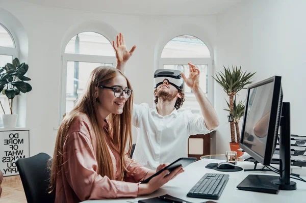 Verspielte Büroangestellte mit Virtual-Reality-Brille und Frau mit Tablet — Stockfoto