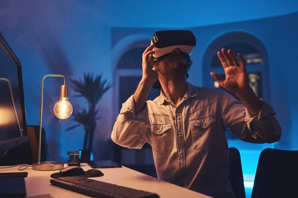 Jongeman zit aan tafel in donkere kamer met virtual reality bril — Stockfoto