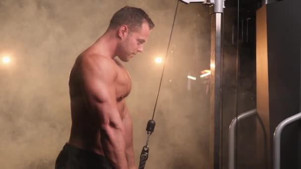 Silný muž pracuje s moderním tréninkovým strojem ve světlé a kouřové tělocvičně — Stock video