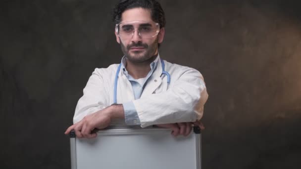 Bearded doctor holding a board in dark background — Stock Video