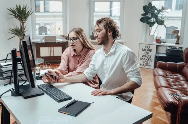 Mannelijke en vrouwelijke collega 's kijken naar telefoon zittend aan tafel in functie — Stockfoto