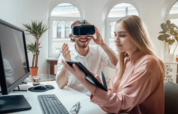 Fröhlicher Kerl genießt Virtual-Reality-Brille, während seine Partnerin am Tablet arbeitet — Stockfoto