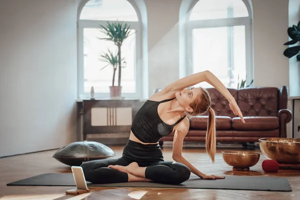 Blanke sportieve vrouw doet yoga met behulp van een mobiele telefoon thuis — Stockfoto