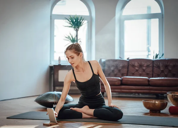 Young sportswoman touches her smartphone sitting on carpet in room — Stock Photo, Image