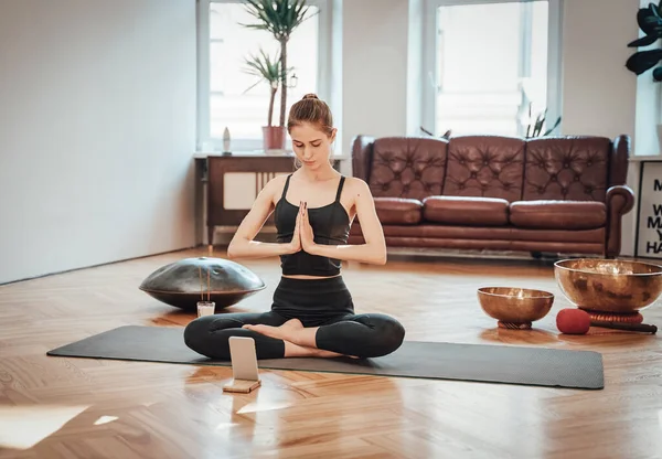 Kaukasiska sportig kvinna gör yoga med hjälp av en mobiltelefon hemma — Stockfoto