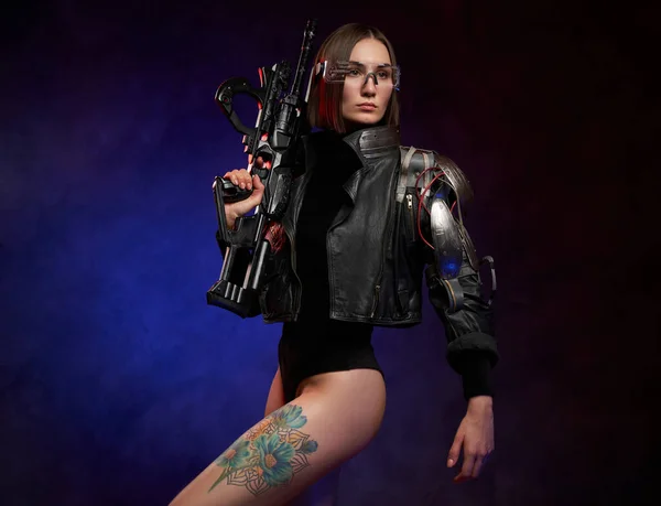 Futuristic cyber woman holding rifle in dark and atmospheric studio — Stock Photo, Image