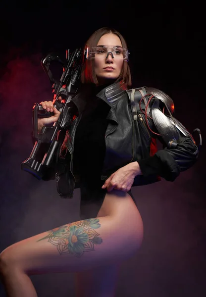 Szexi és karcsú nő implantátummal és puskával pózol sötét háttérben — Stock Fotó