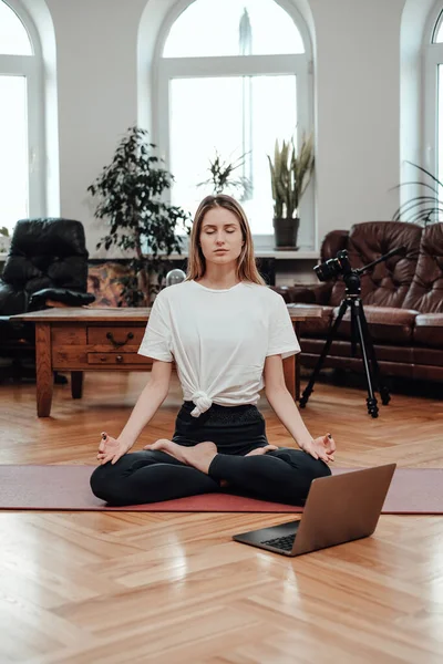 Young female athlete with laptop relaxes doing yoga in room — Stock Photo, Image