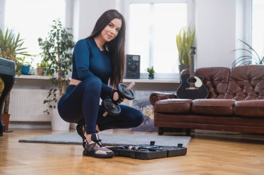 Neşeli kadın vücut geliştirici spor malzemelerini odada hazırlıyor.