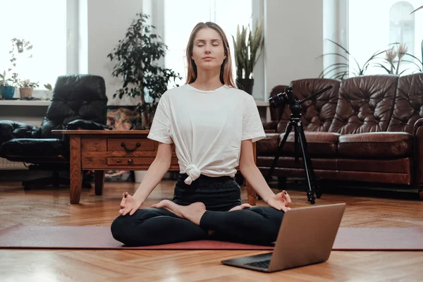 Młoda atletka z laptopem relaksuje się uprawiając jogę w pokoju — Zdjęcie stockowe