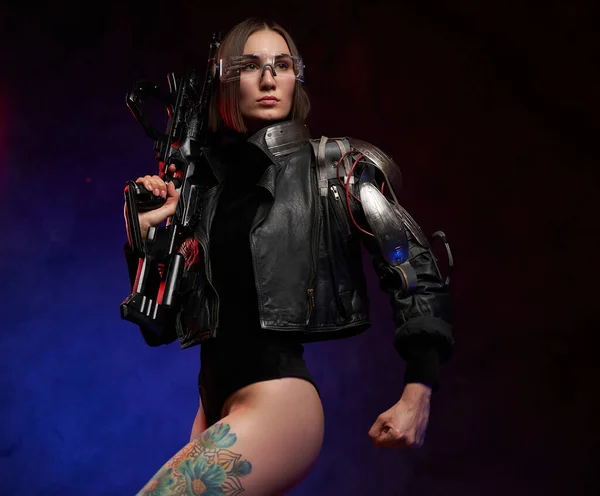 Mulher com braço cibernético posa com rifle em fundo escuro — Fotografia de Stock